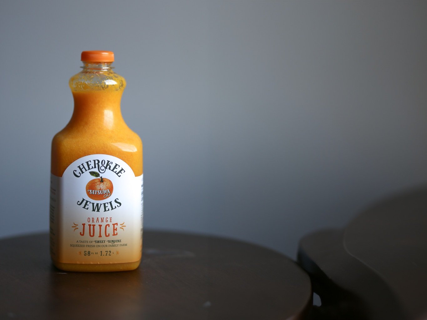 Bottle of Cherokee Jewels orange juice made from Satsuma oranges, placed on a wooden table against a gray background, showcasing its vibrant color and label design.